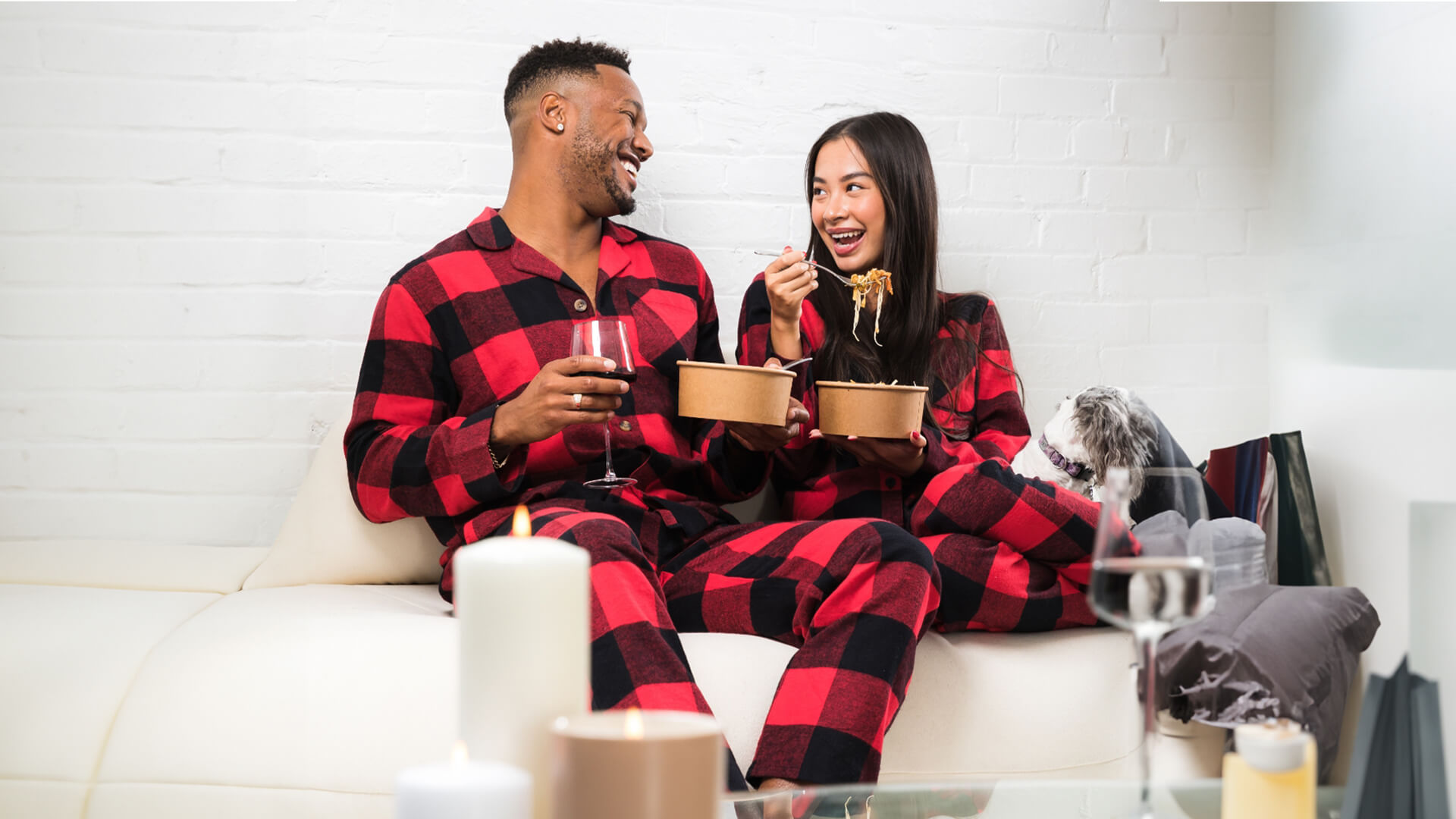 Couple in matching pajamas enjoying dinner and a glass of red wine.